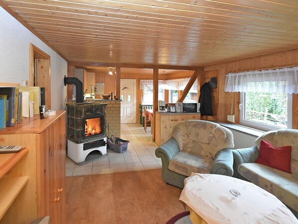 A cozy cabin interior with a fireplace, wooden furniture, and a view through a window. - Welcoming Bungalows in Neustadt (Harztor)