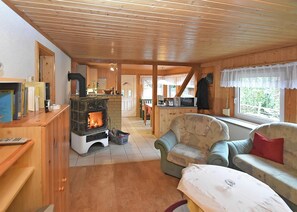A cozy cabin interior with a wood-burning stove, a dining area, and a living room with a sofa and a table. - Welcoming Bungalows in Neustadt (Harztor)