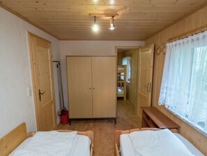 A room with two wooden beds, a wardrobe, a bench, and a window with lace curtains. - Welcoming Bungalows in Neustadt (Harztor)