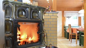 A kitchen with a wood-burning stove, a brick wall, and a dining area with a table and chairs. - Welcoming Bungalows in Neustadt (Harztor)