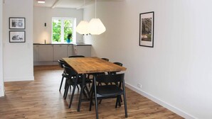 A dining area with a wooden table and black chairs, a kitchen in the background, and framed pictures on the walls. - 4 Person Holiday Home in Svaneke (Svaneke)