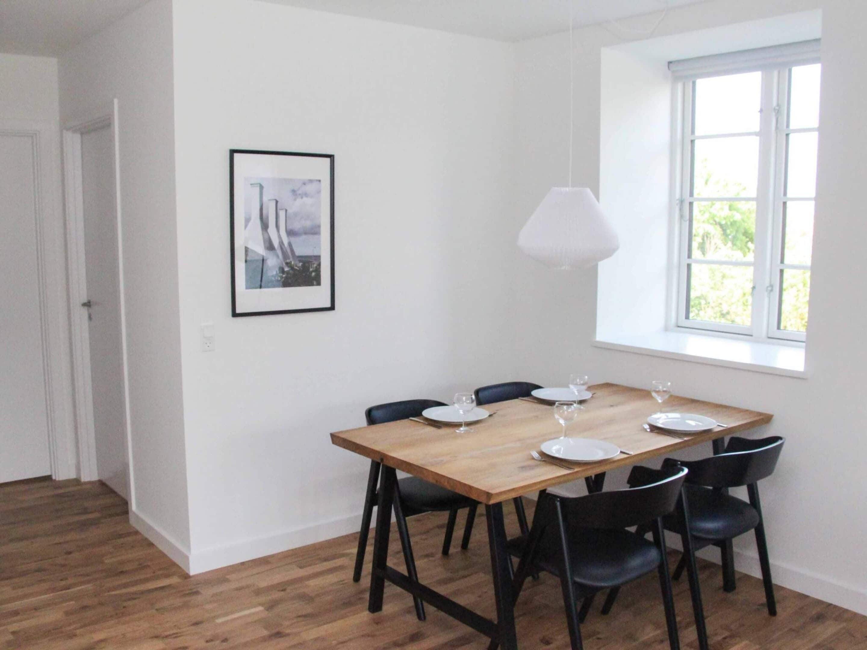 Un espace repas avec une table en bois, des chaises noires et un luminaire suspendu blanc.