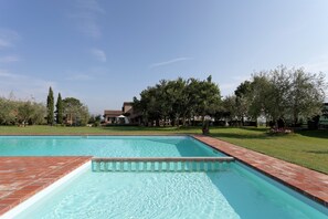 Ein rechteckiger Pool mit Backsteinrand, umgeben von einem gepflegten Rasen und Bäumen.