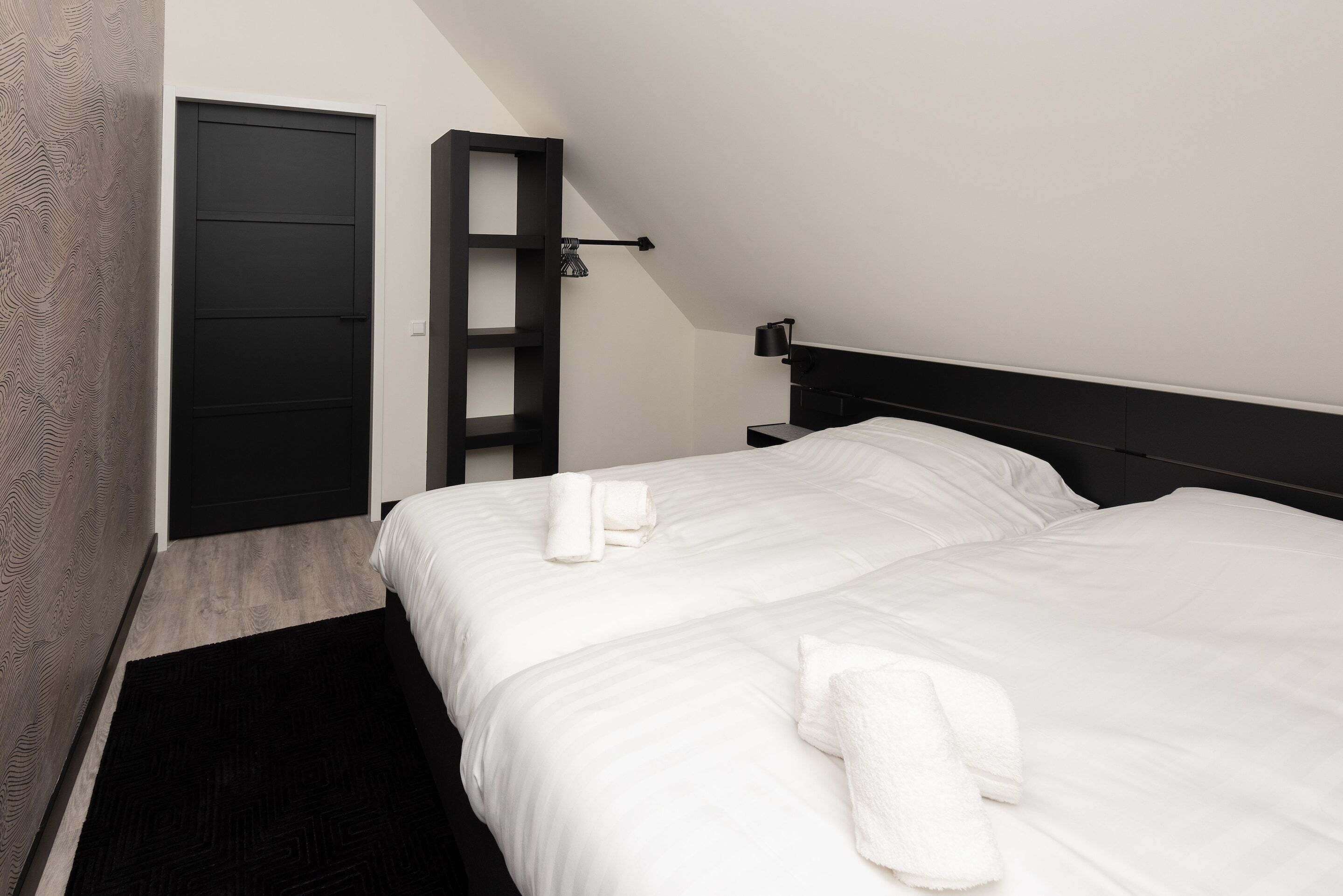 A modern hotel room with a large bed, a black headboard, and a built-in shelf.