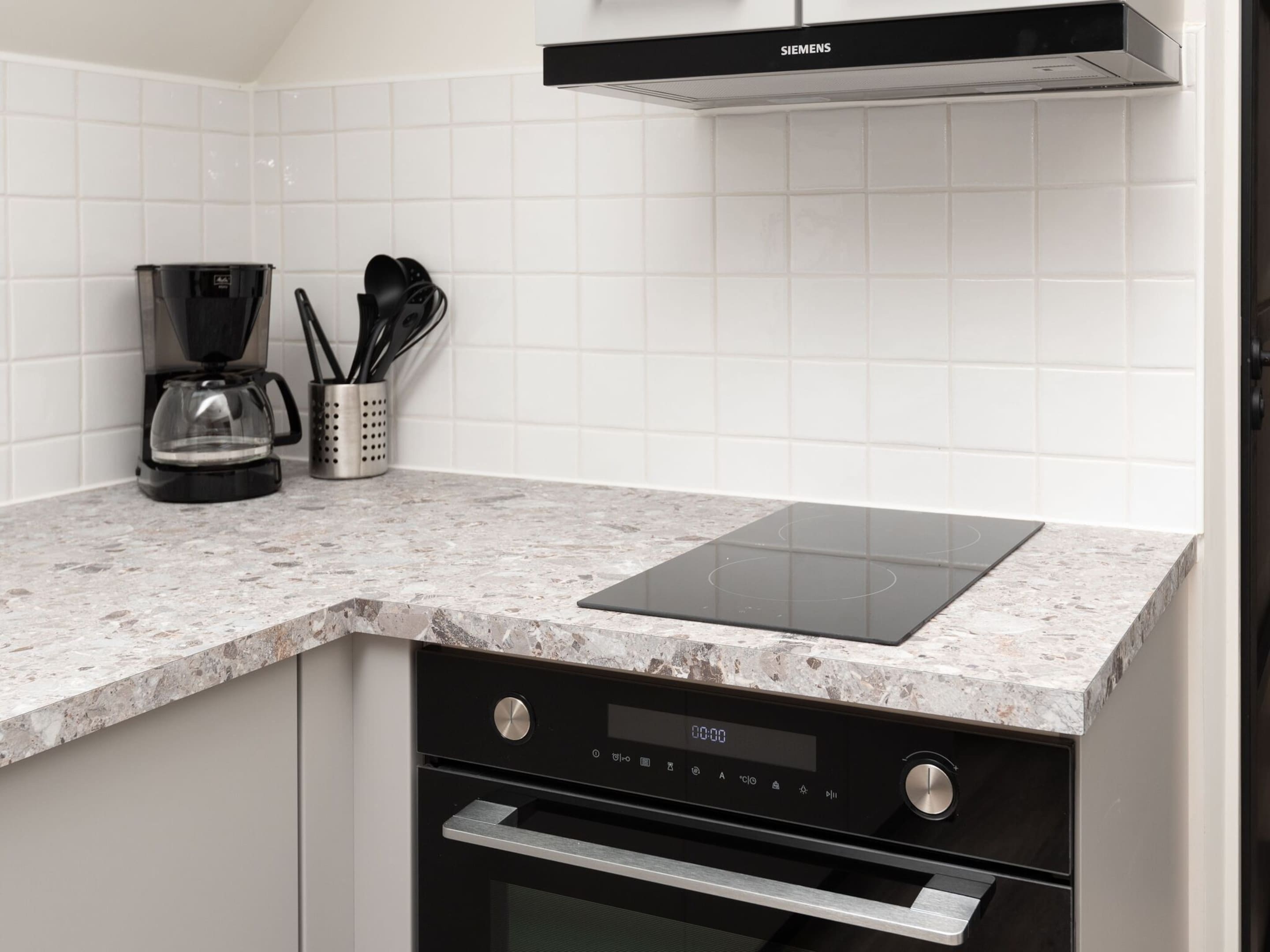 A modern kitchen with a built-in stovetop, a coffee maker, and a utensil holder.