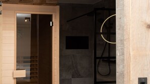 Un baño moderno con cabina de ducha de vidrio, puerta de madera y toallero negro.
