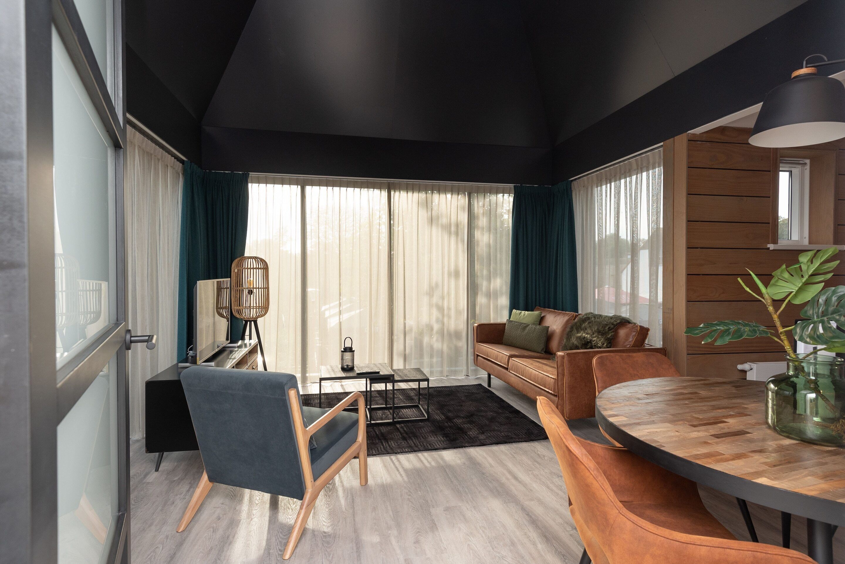 A modern living room with a dark ceiling, a wooden dining table, a sofa, and a chair.