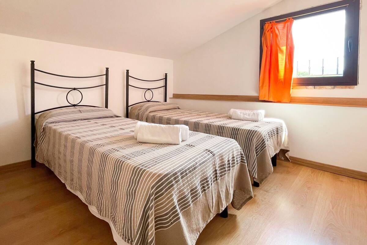 A room with two beds, a window with curtains, and a wooden floor.