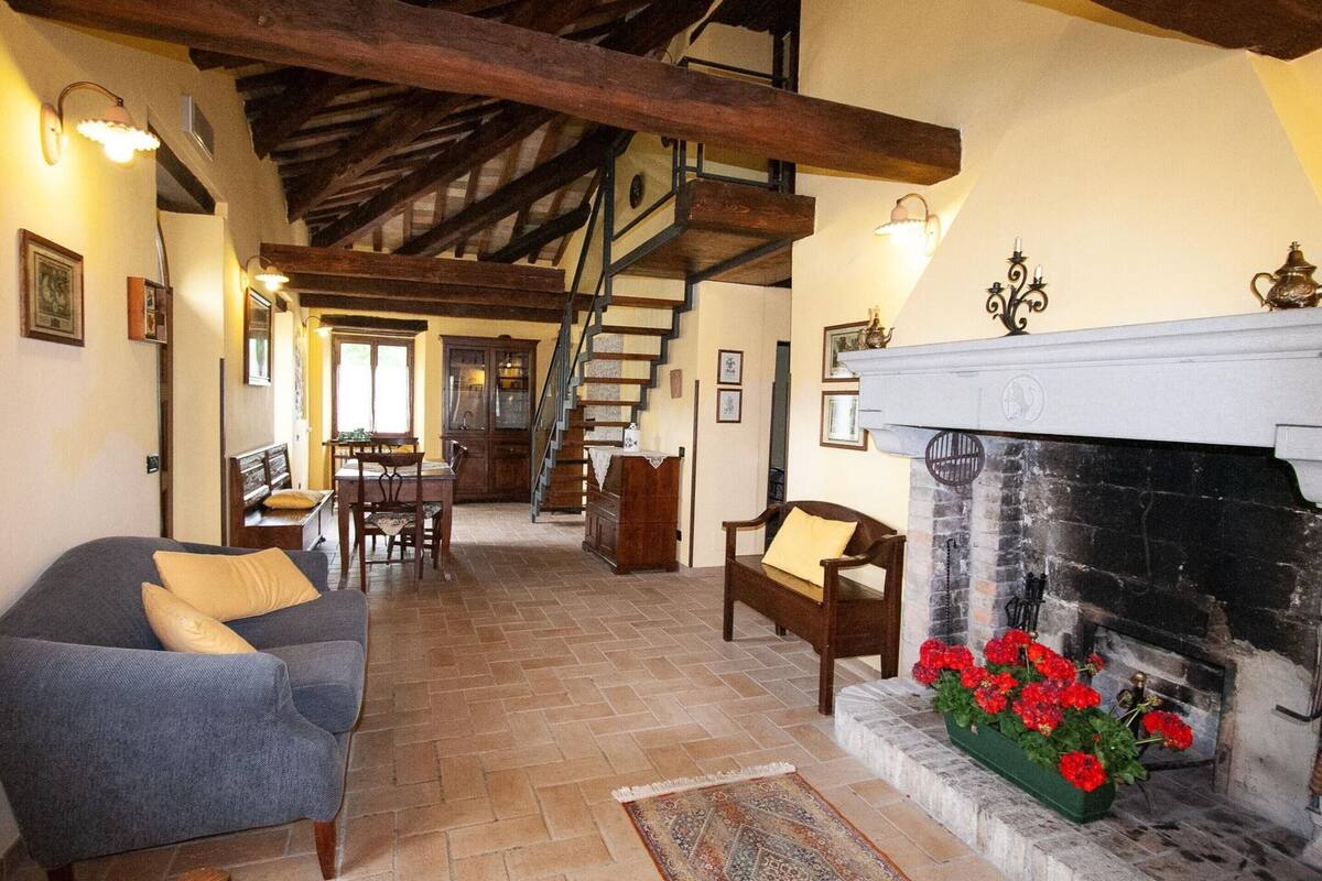 A spacious living area with a fireplace, wooden beams, a staircase, and a dining area.