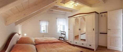 A bedroom with a wooden ceiling, a bed with multiple pillows, a wardrobe, and a chair.