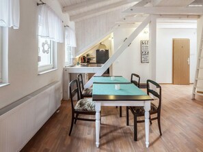 A dining area with a table and chairs, a kitchen in the background, a staircase, and a door with a sign. - Modernes Ferienhaus in der Nahe des Waldes in Thale (Thale)