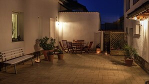Un patio con mesa y sillas de madera, plantas en macetas y un banco.