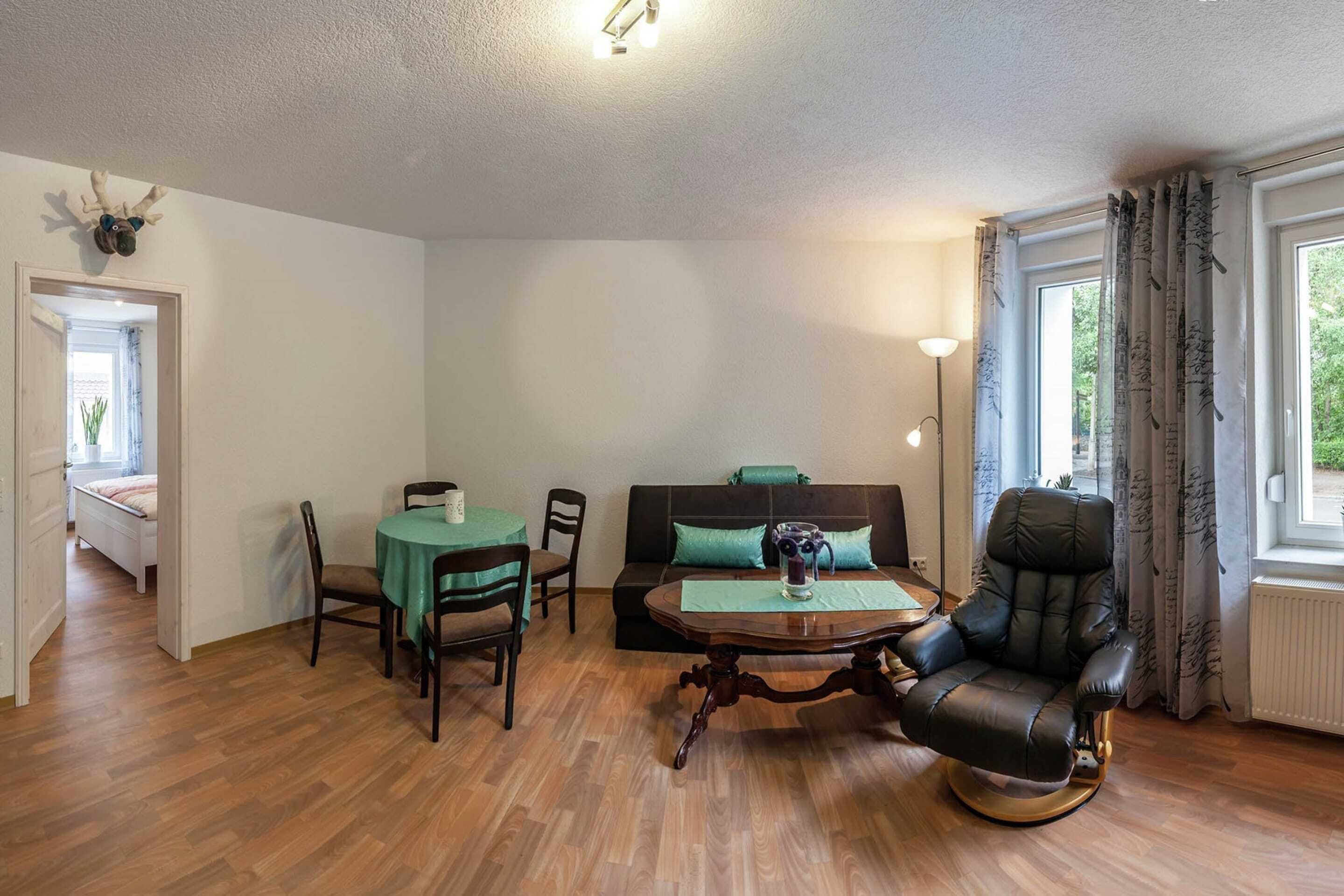 Una habitación con una mesa de comedor, sillas, un sofá, un sillón de masaje, un adorno de cabeza de venado en la pared y una ventana con cortinas.