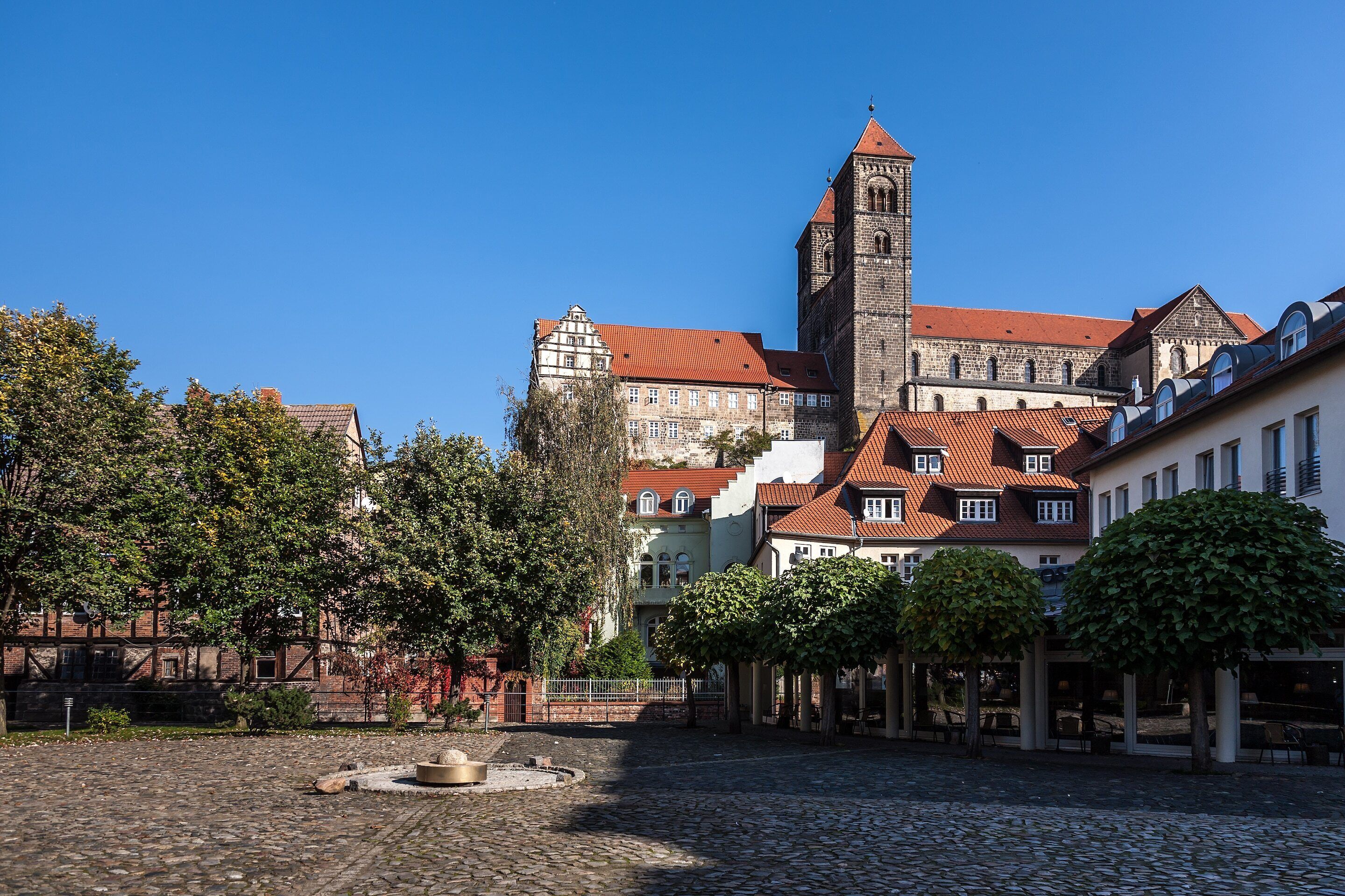 Ein historisches Gebäude mit einem markanten Turm, einem Innenhof mit Brunnen und umliegenden Bäumen.