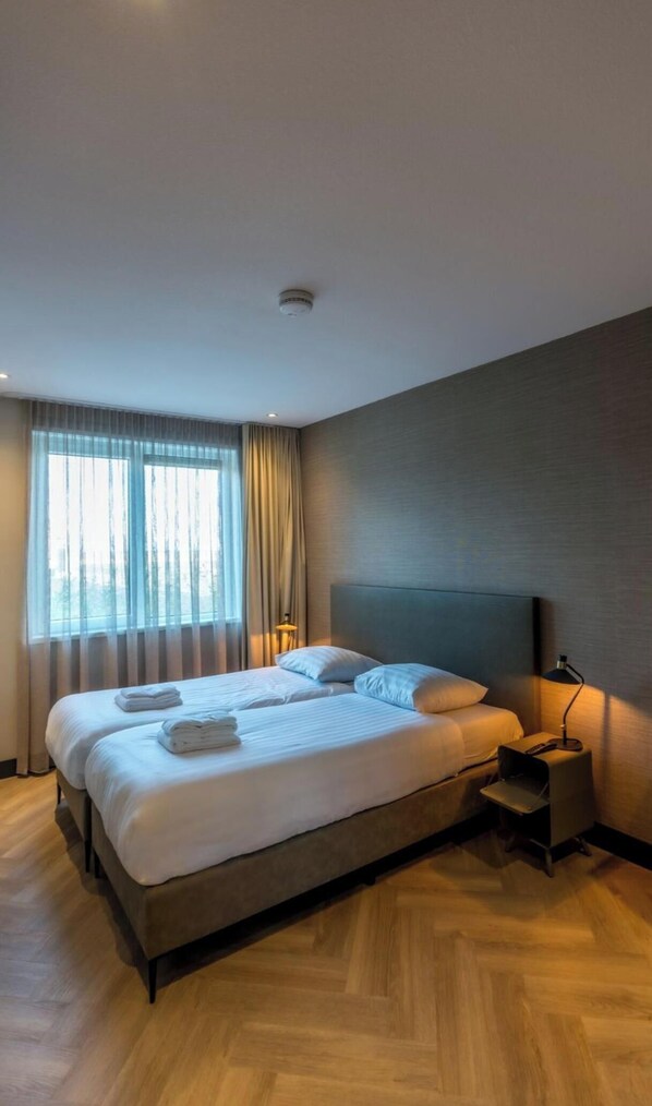 A modern hotel room with a large bed, a bedside table, a lamp, and a view through the window. - Modern Villa in De Cocksdorp Near the Beach (De Cocksdorp)