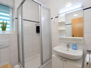 Un baño moderno con cabina de ducha de vidrio, un lavabo blanco con espejo y una planta en maceta en el alféizar de la ventana.