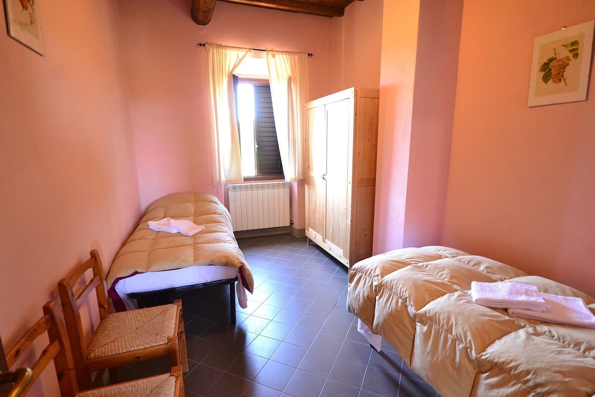 A small, cozy bedroom with two single beds, a wooden wardrobe, a radiator, and a window with curtains.