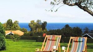 Two striped lounge chairs with white cups on a grassy lawn, overlooking a body of water and trees. - 2 Person Holiday Home in Allinge (Allinge)