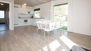 A modern kitchen with white cabinets and a dining area with a white table and chairs. - 8 Person Holiday Home on a Holiday Park in Blavand (Blavand)