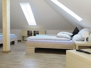 Camera da letto con soffitto spiovente, lucernario, struttura del letto in legno, biancheria a motivi decorativi, comodini e telecomando.
