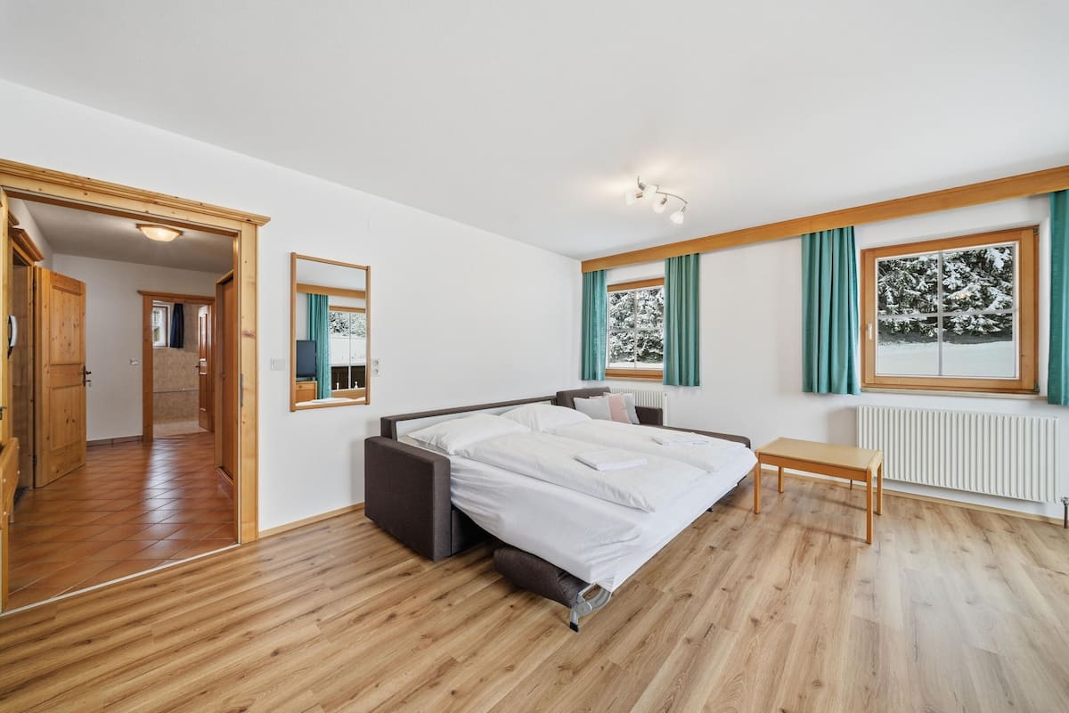 A bedroom with a bed, a bedside table, a window with curtains, and a view of a snowy landscape.
