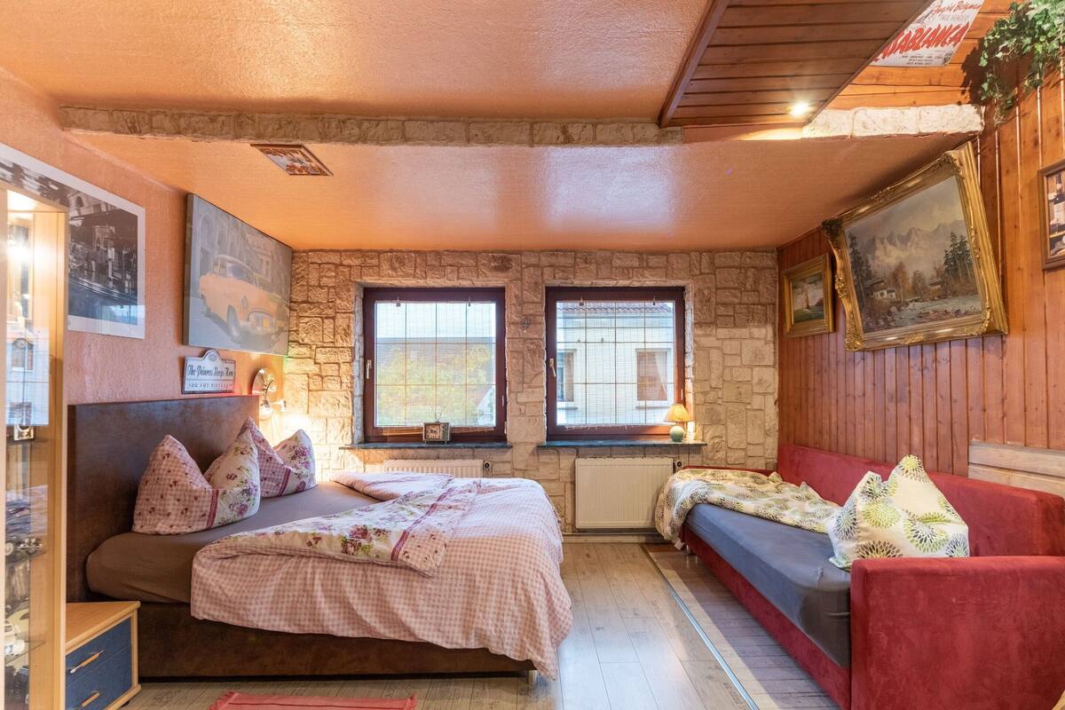 A cozy bedroom with a bed, a red sofa, stone walls, and framed pictures.