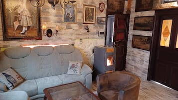 A cozy living room with a stone wall, a sofa, a chair, a fireplace, and various framed pictures.