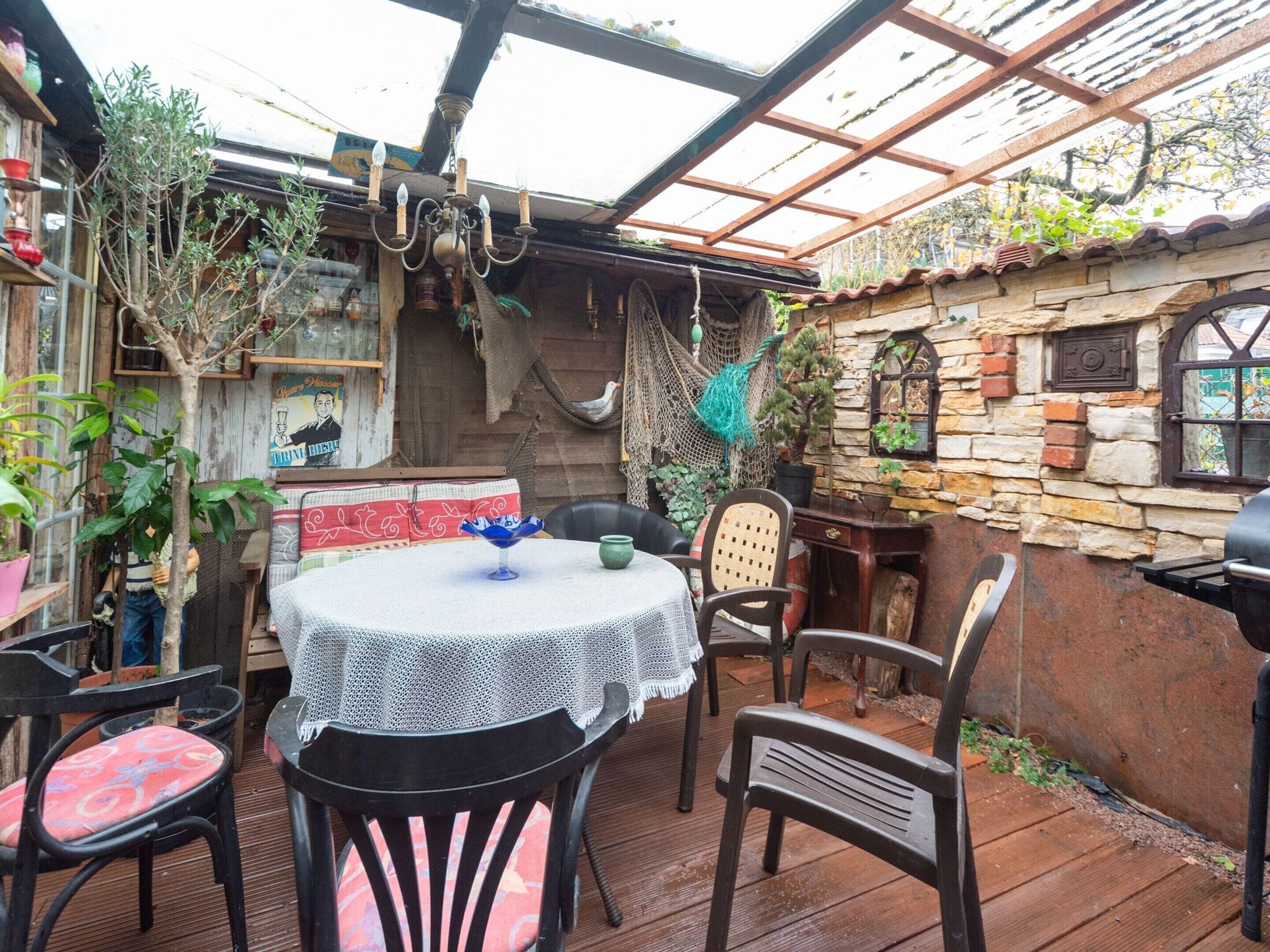 A covered patio area with a table and chairs, surrounded by stone walls and potted plants.