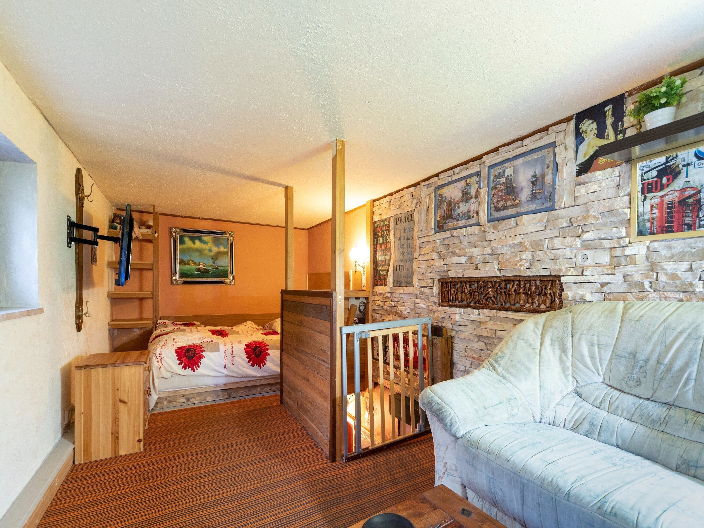 A cozy room with a bed, a wooden cabinet, a white sofa, and a stone wall with framed pictures.