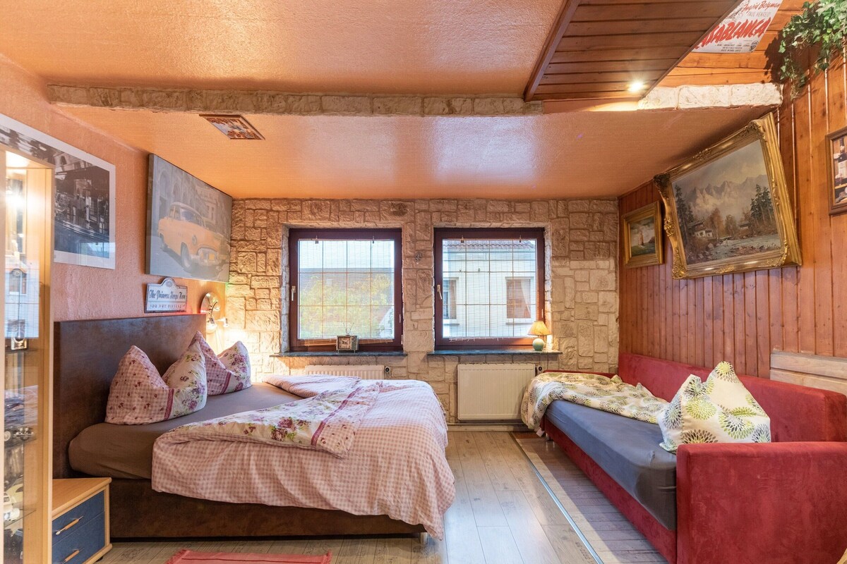 A cozy bedroom with a bed, a red sofa, stone walls, and framed pictures.