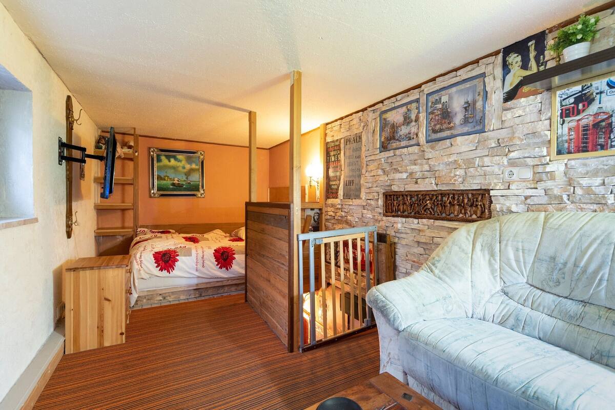 A compact room with a bed, a wooden cabinet, a white sofa, and a stone wall with various framed pictures.