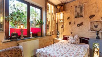 A room with a bed, a window with plants, a radiator, and a wall with various decorations.