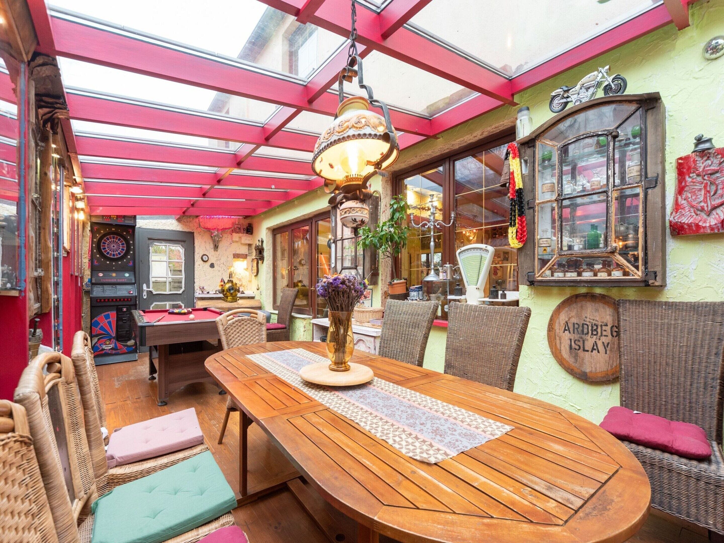A cozy indoor dining area with a wooden table, wicker chairs, and a glass ceiling.