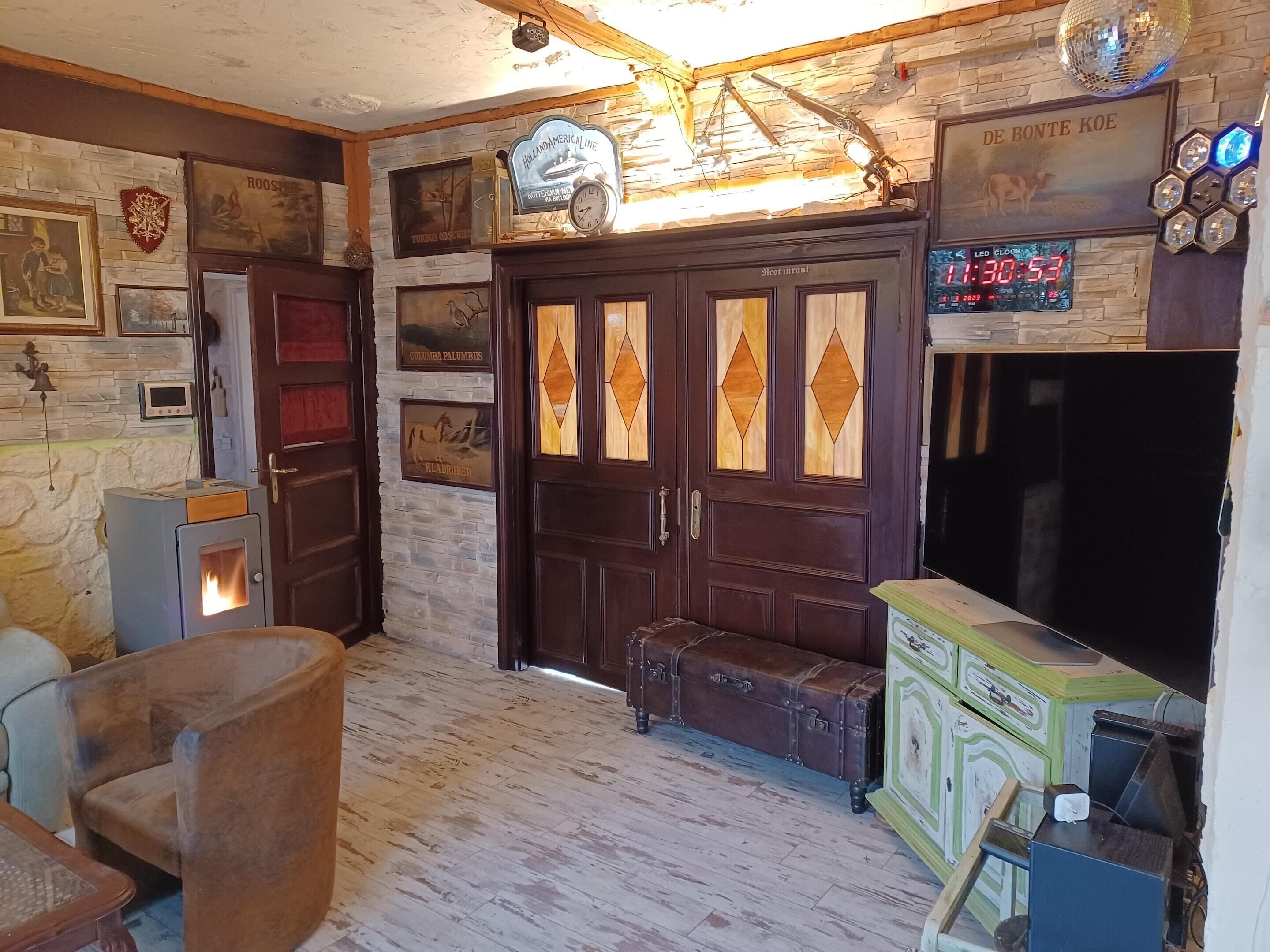 A cozy room with a stone wall, wooden door with diamond patterns, a vintage suitcase, a small heater, and a clock displaying 1:30:53.