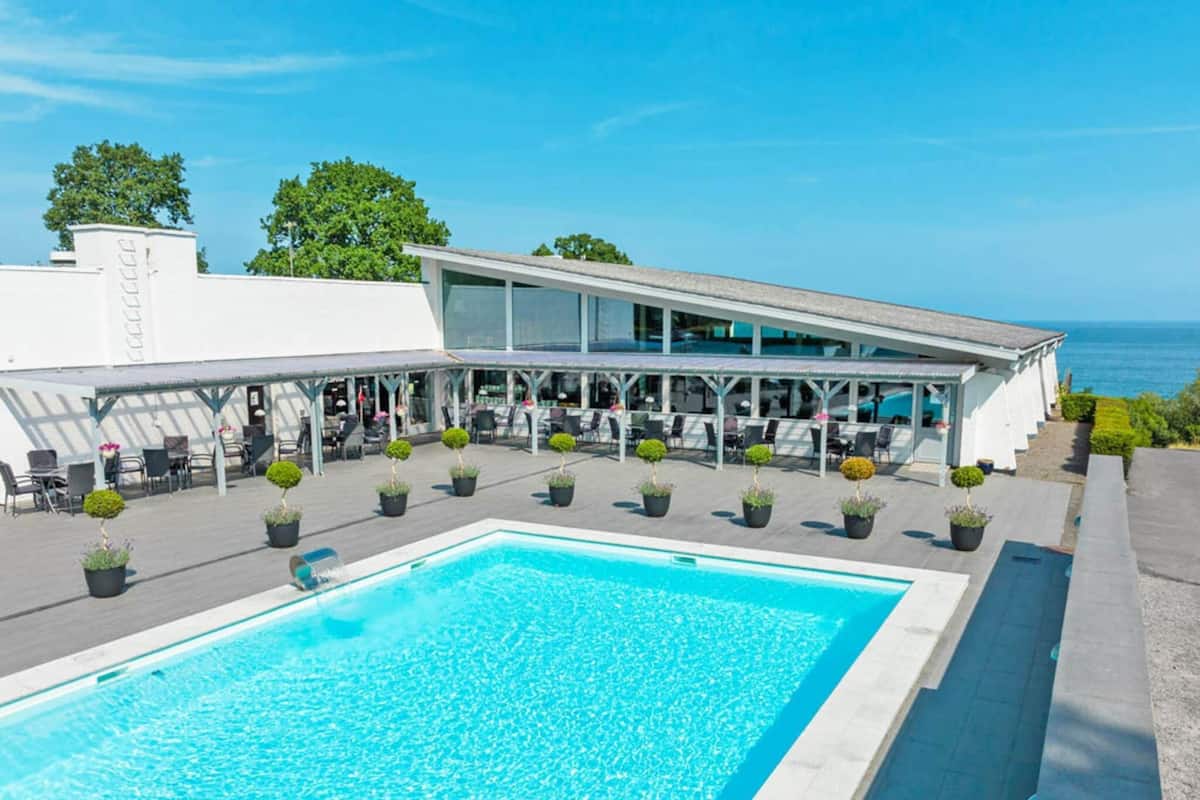 A modern hotel with a pool, outdoor seating, and a view of the sea.