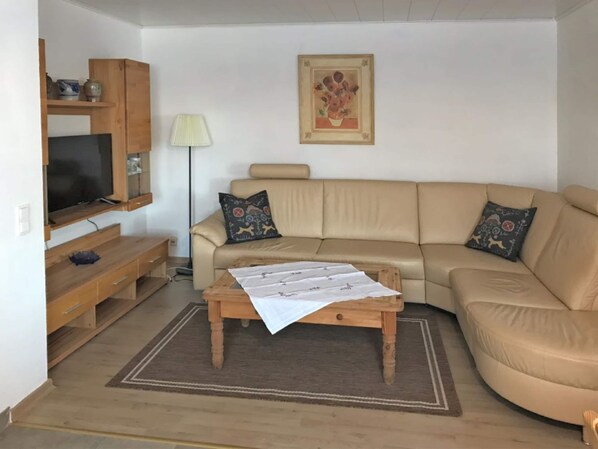 A living room with a beige sofa, a wooden coffee table, a television on a wooden stand, and a lamp.