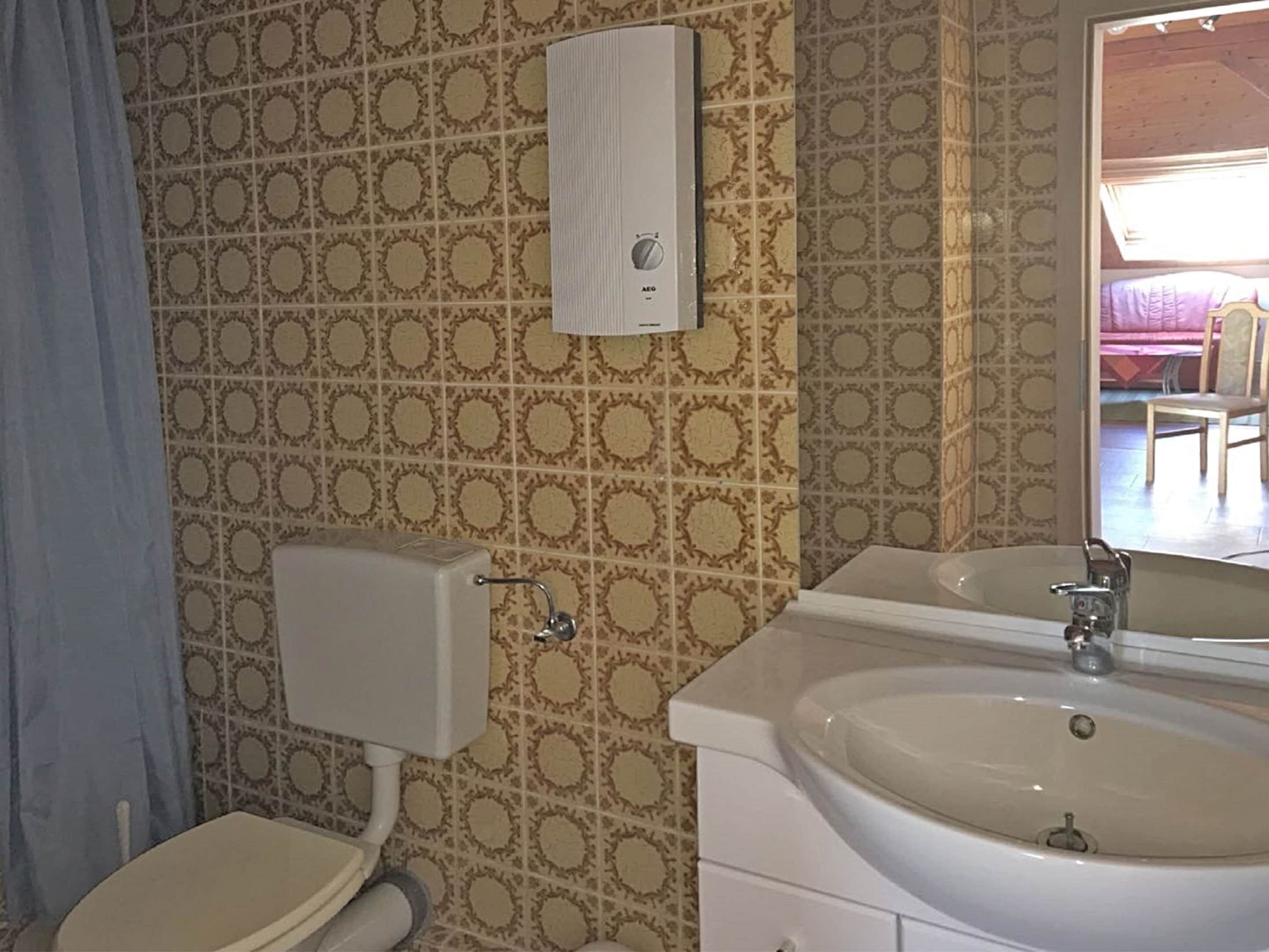 A bathroom with patterned tiles, a toilet, a sink with a mirror, and a towel dispenser.