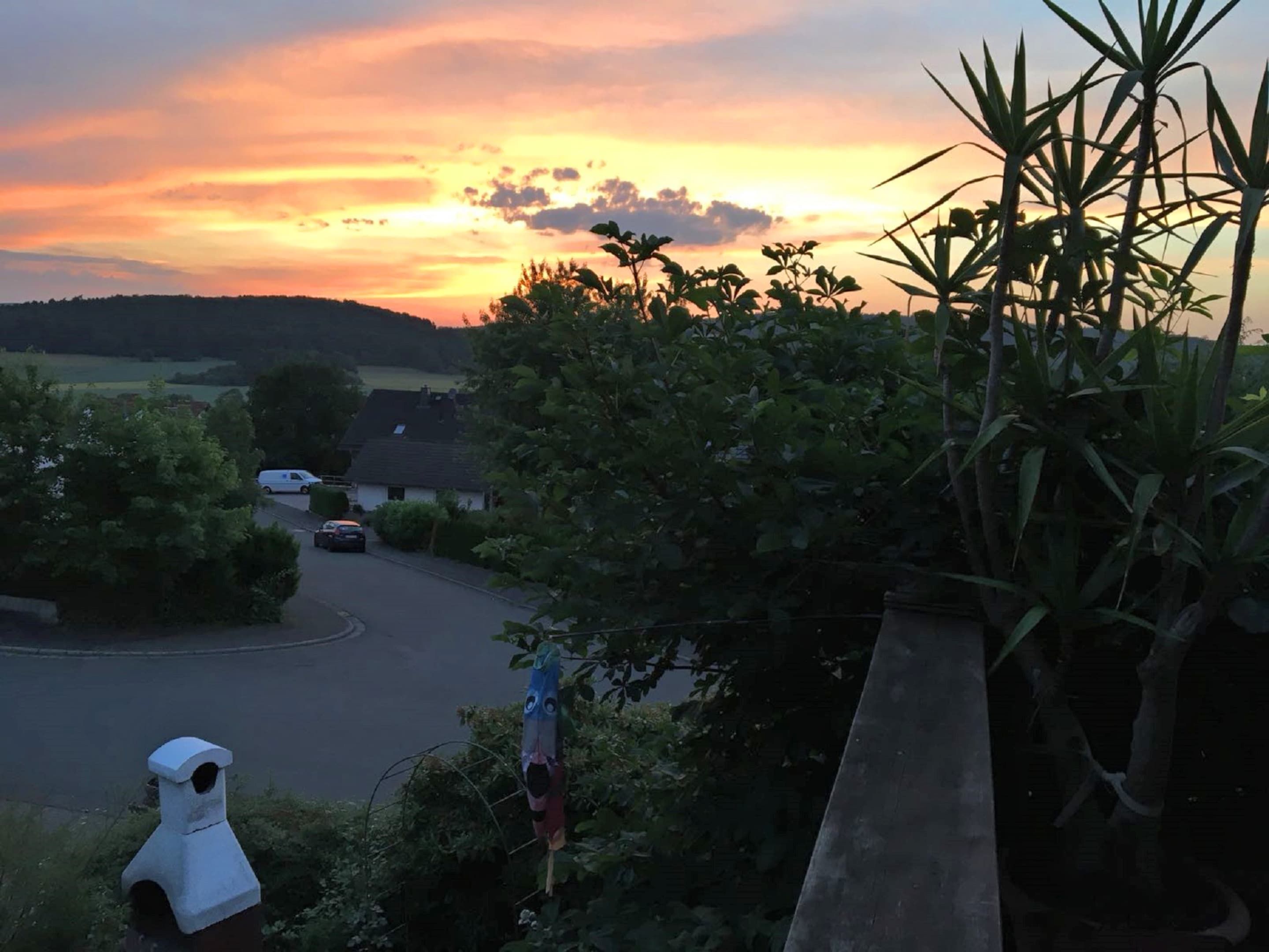 Área residencial com estrada, carros estacionados e pôr do sol.