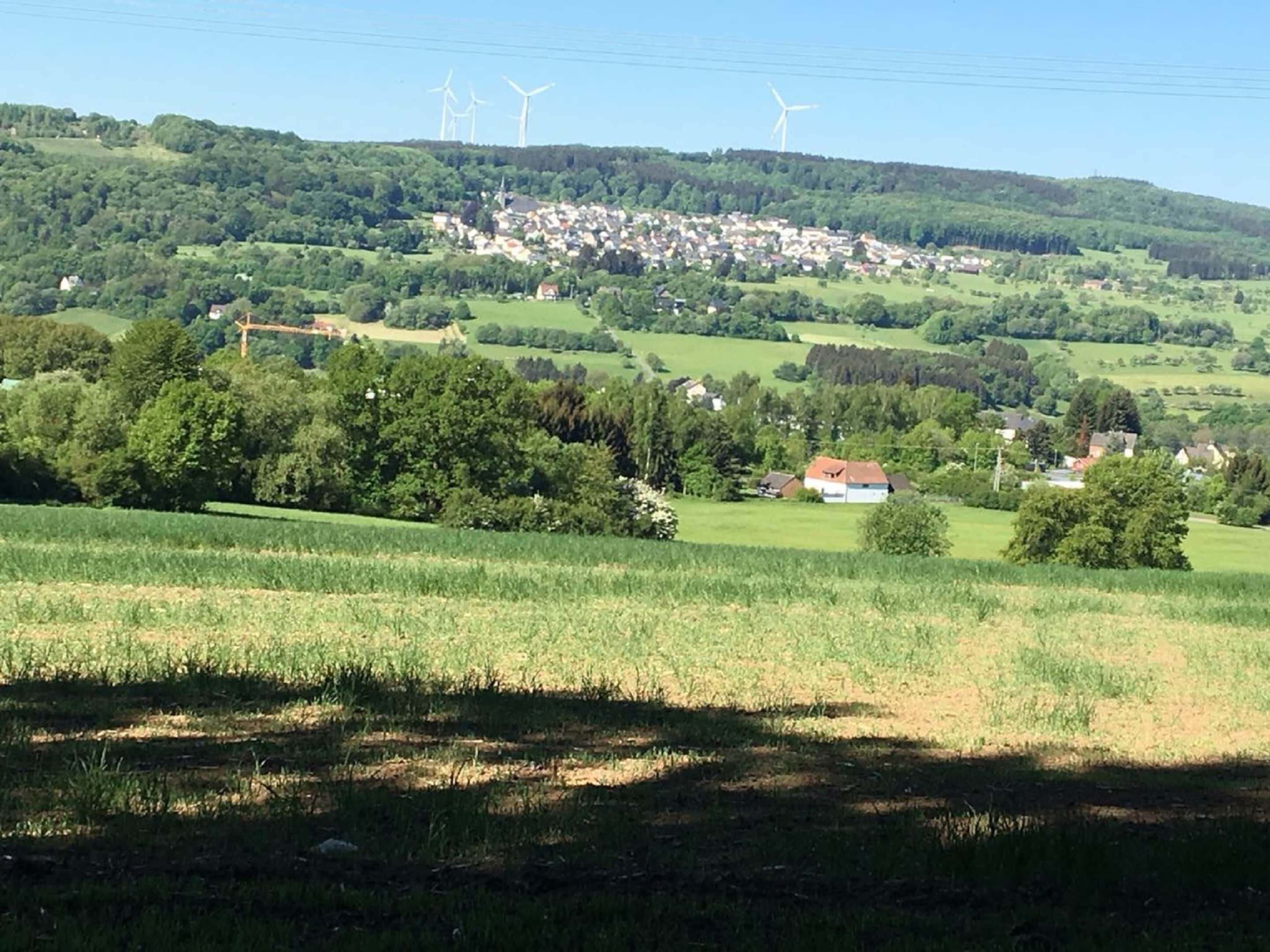 Un paysage rural avec des éoliennes, un petit village et des champs verdoyants.