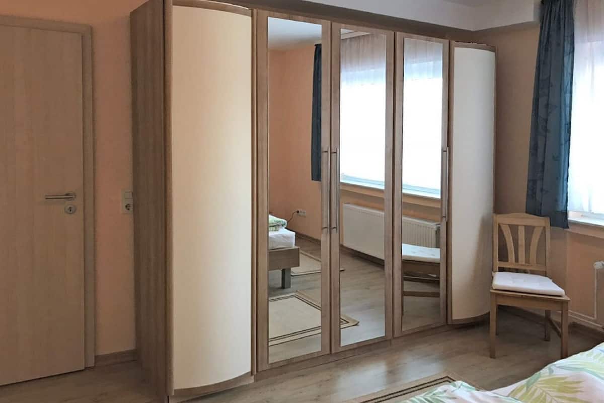 A bedroom with a wardrobe, a bed, a chair, and a window with curtains.