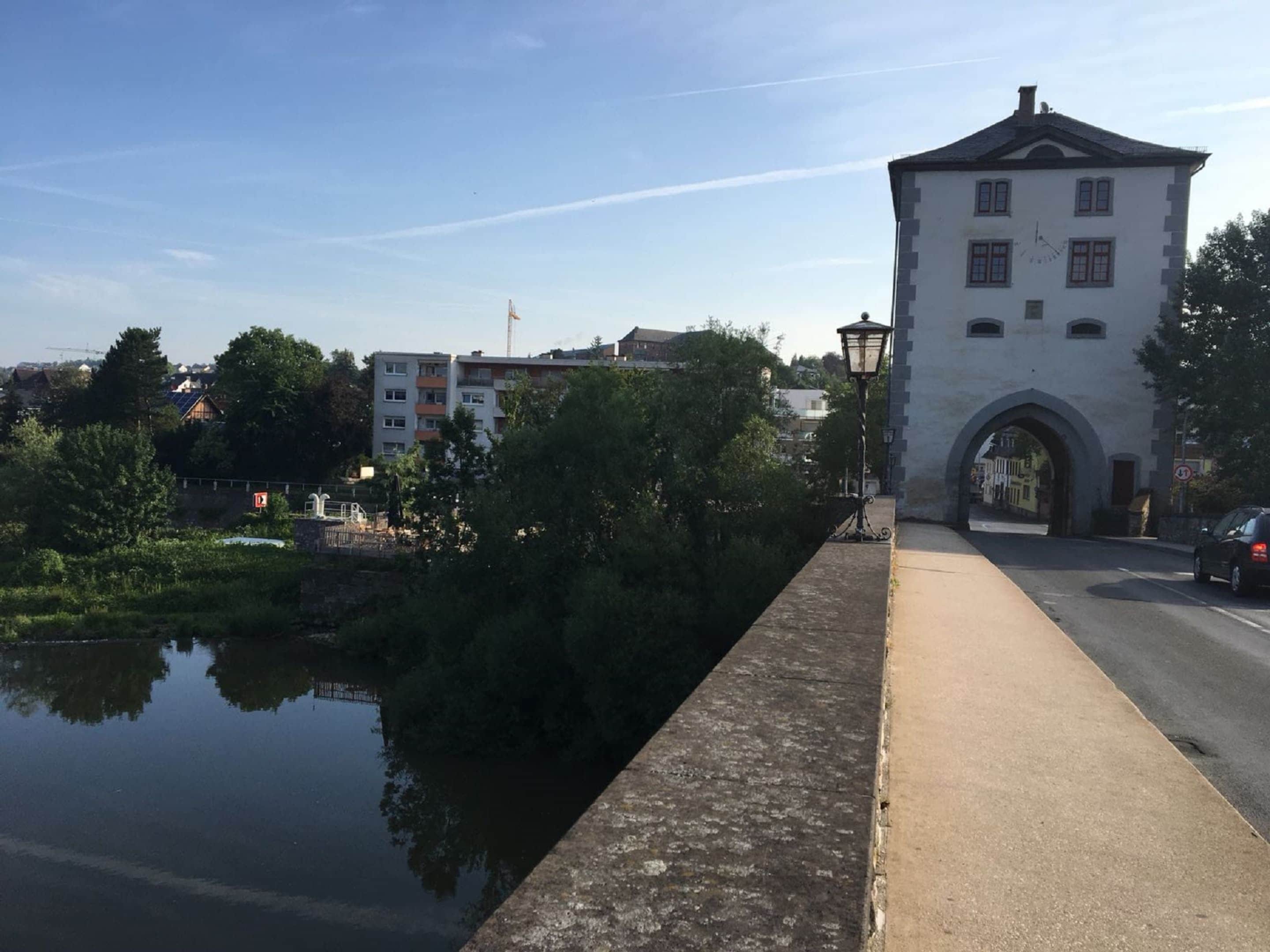 Un bâtiment historique doté d’un clocher, d’un pont et bordé par une rivière paisible.