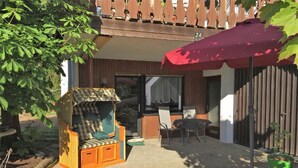A patio area with a wicker sofa, a table, and chairs, a red umbrella, and a wooden fence.