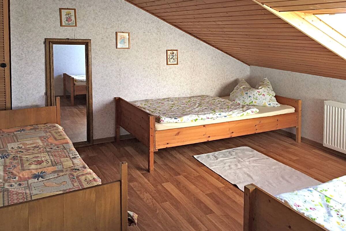 A small, cozy room with a wooden bed, a small table, and a window with a sloped ceiling.