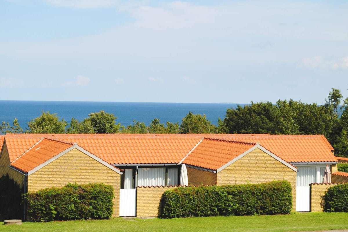 A row of brick buildings with orange tiled roofs, white window frames, and a view of the sea.