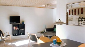 A modern living room with a flat-screen TV, a bookshelf, a dining table with chairs, and a large painting on the wall. - 4 Person Holiday Home in Allinge (Allinge)