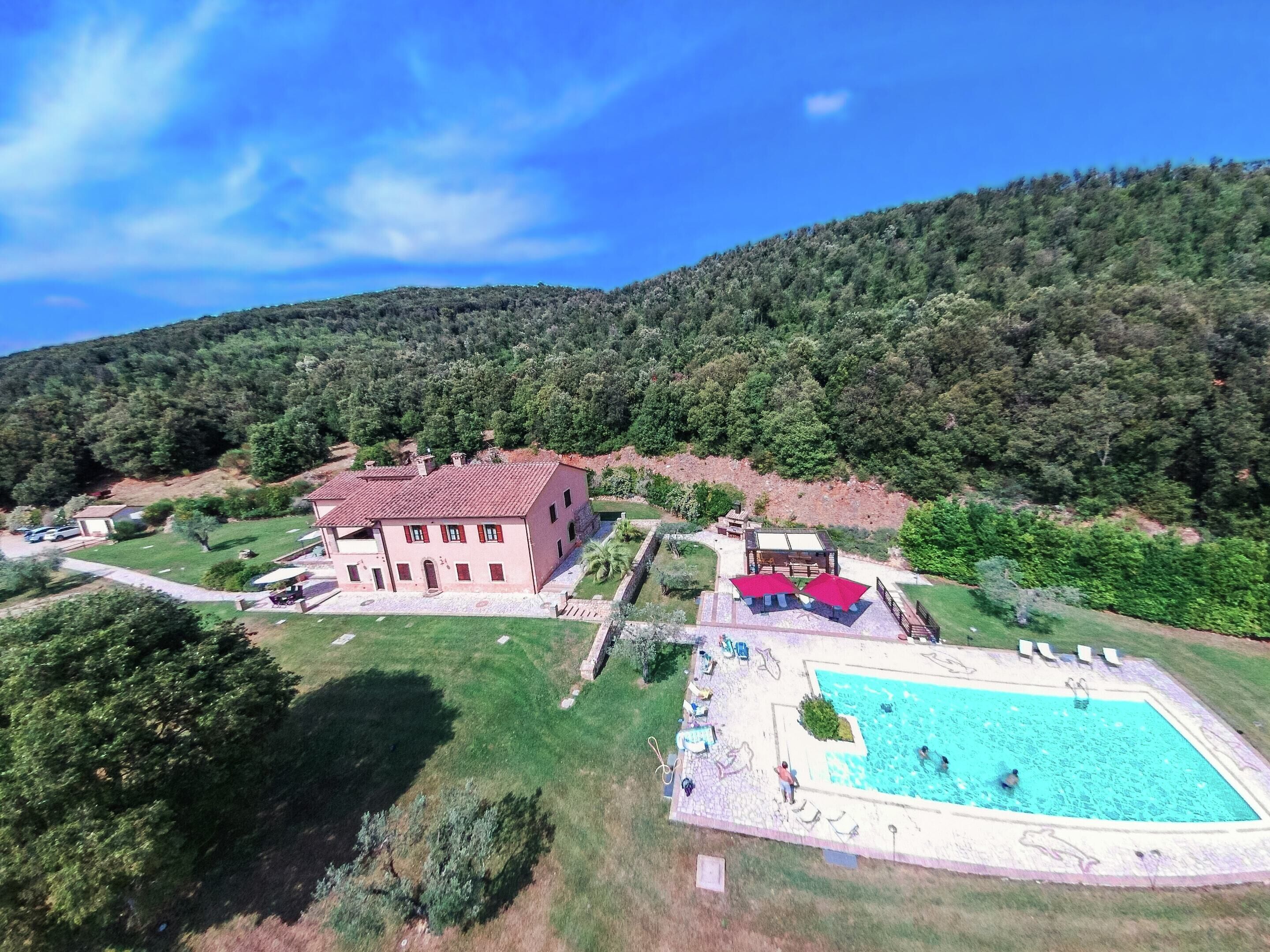 A large house with a swimming pool, surrounded by a well-maintained lawn and a forested hillside.