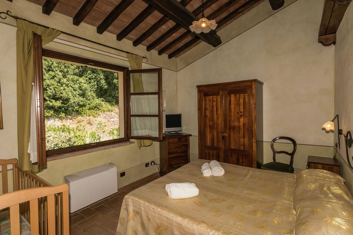 A bedroom with a bed, a wooden wardrobe, a desk with a computer, a chair, and a window with curtains.