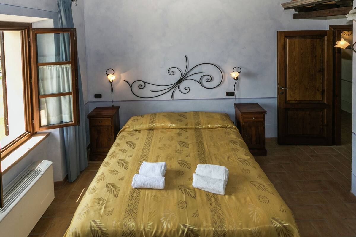 A bedroom with a bed, two bedside tables, a window, a radiator, and a door.