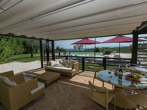 An outdoor patio with wicker furniture, a glass table with wine glasses and fruit, and a view of a pool and mountains. - Elegant Apartment Only 1 Hour From Rome (Narni)
