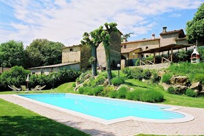 Una piscina con sillas de descanso, rodeada de vegetación y edificios de piedra.